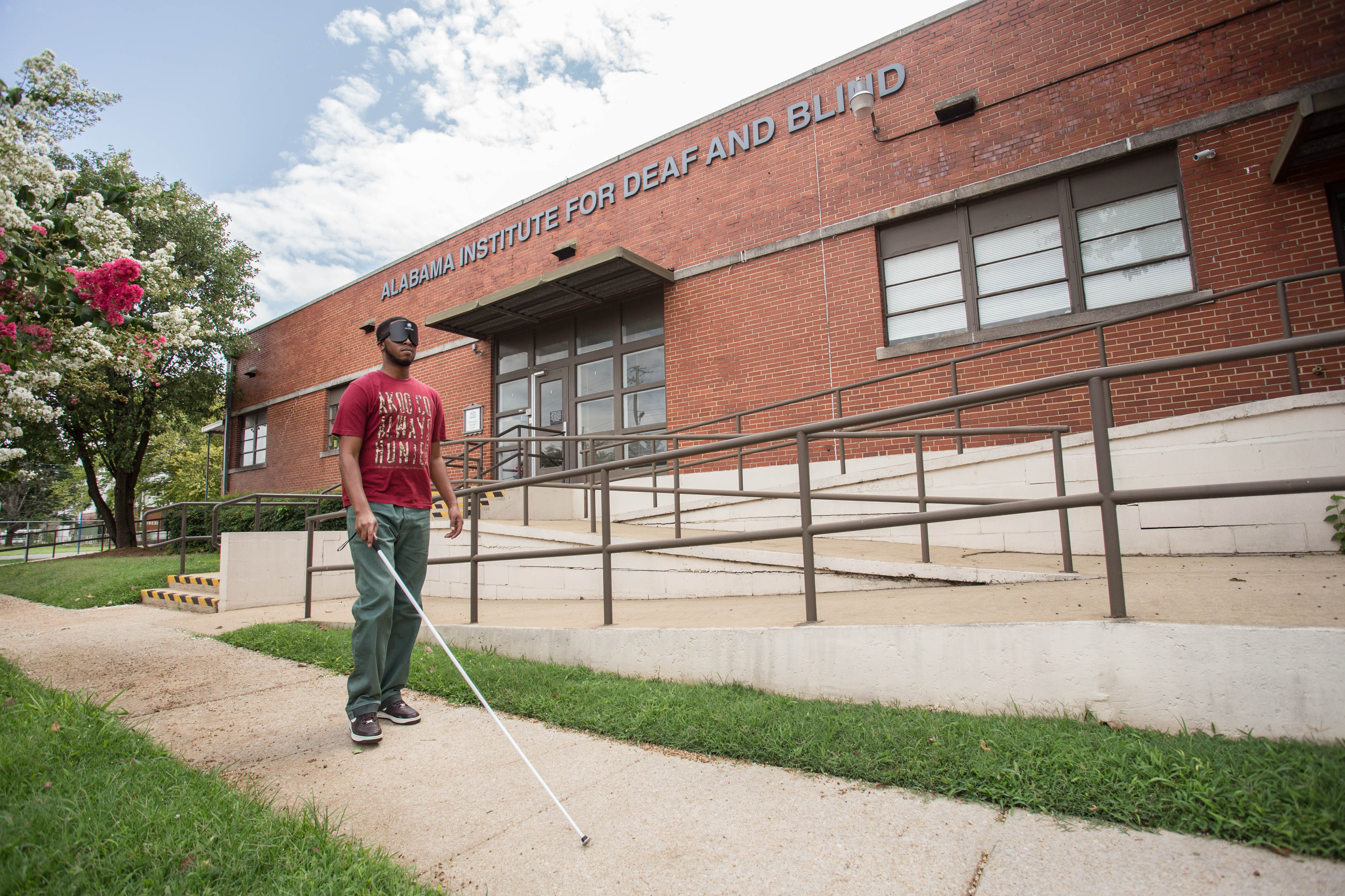 The entrance of the AIDB Birmingham Regional Center a red brick building with a blind student under learning shades walking The entrance of the AIDB Birmingham Regional Center a red brick building with a blind student under learning shades walking